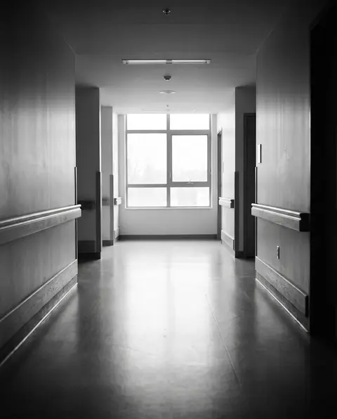 Quiet, empty hospital rehabilitation corridor with soft daylight from a window at the far end